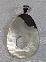 Front view of the sterling silver and mother of pearl pendant with circular cutout on fabric background.