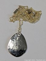Close-up of the hammered teardrop-shaped silver pendant and a portion of the chain.