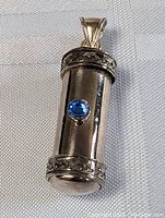 Front view of cylindrical vintage silver keepsake pendant with a central blue stone and decorative end bands.