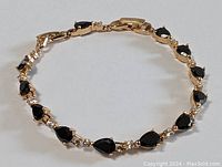 Close-up of gold plated bracelet showing pear-shaped black onyx stones with small clear crystals between each.
