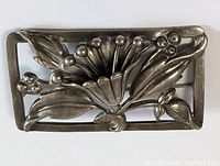 Close-up front view of rectangular silver-toned Art Nouveau brooch with raised floral and leaf motifs, with dark patina.