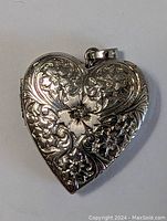 Front view of the antique heart-shaped silver locket pendant with floral engraving and diamond center.