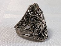 Close-up photo of the ring showing the detailed filigree design on the front, with visible patina.