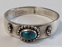 Front and slightly angled side view showing oval turquoise centerpiece with silver bead detailing on sterling silver band.