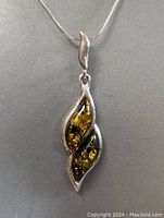 Close-up of amber pendant showcasing natural inclusions inside polished amber, set in sterling silver leaf design with curved shape