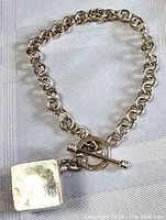 Clear photo showing entire sterling silver chain with toggle clasp and attached square box charm on a light cloth background.