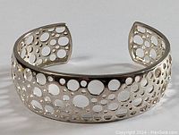 Side angled view of the sterling silver modernist cutout bracelet lying on a white surface showing the circular openwork pattern and polished finish.