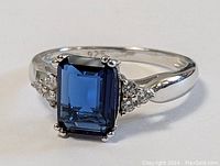 Close-up view of the sterling silver ring showing the emerald-cut blue stone and flanking clear stones.