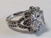 Close-up side angle view of the sterling silver ring with large square clear stone and smaller accent stones along the band and ornate setting.