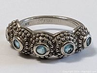 Close-up angled view of the sterling silver ring showing five round blue stones set in beaded bezel settings with a scalloped pattern on top.