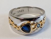 Close-up front view of sterling silver ring showing dark blue triangular stone, smaller round light blue stone, gold-tone accents, and 5925 silver mark inside band.