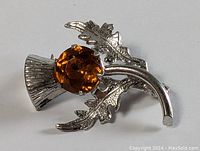 Close-up image of the sterling silver thistle brooch showing amber-colored faceted stone and leaf details.