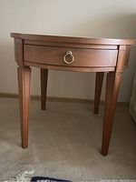 Front view of one side table showing drawer with metal ring pull and tapered legs