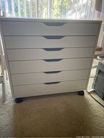 Front view of white 6-drawer art table showing drawer handles and caster wheels.
