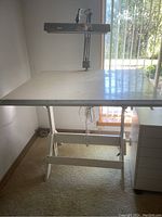 Full view of white artist table with overhead light, shows base and table surface angle.