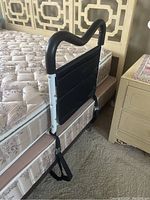 Single bed rail set up on side of a bed showing padded handle, black fabric pocket, and securing straps.