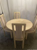 Photo of the cream coloured round dining table with 4 chairs arranged around it. The table surface is smooth with a glossy finish and light cream colour.