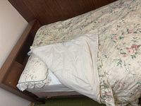 Bed with wooden headboard, floral mattress, and pillow with white fitted sheet partially removed.
