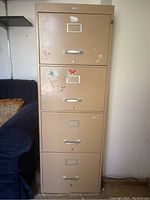 Front view of beige 4 drawer metal filing cabinet with visible wear and assorted stickers on drawer fronts.