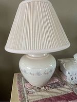 Front and side view of night table lamp showing the ceramic base with floral decoration and pleated beige lampshade.