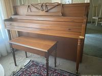 Front view of Schubert upright piano with attached music stand and matching bench in front.