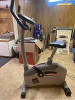 Side view of grey Schwinn exercise bike showing seat, handlebar with digital display, and frame.