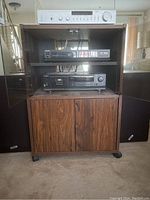 Full front view of sound system showing amplifier, CD player and cassette player inside wooden cabinet with speakers on each side.