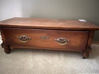 Front view showing the large single drawer with two ornate metal handles and carved legs.