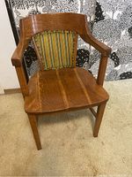Front view of wooden arm chair showing upholstered backrest with striped fabric and solid wooden seat.