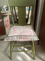 Full view of the green wooden chair with pink cushion from the front, showing the chair's backrest and turned legs.