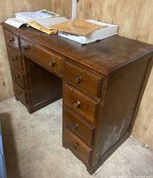 Wooden desk with nine drawers, showing the front and left side with evident wear on finish and some scuff marks on the side.