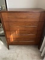 Front view of four-drawer wooden dresser showing integrated handles and medium brown finish.