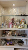 Full view of shelves with assorted glassware, ceramic figurines, decorative Easter themed items, candles, and silver plated crumb-catcher