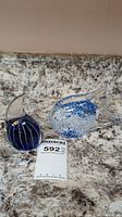 Two art glass fish figurines on a marble surface, blue and clear glass with fin details, shown with Maxsold lot tag
