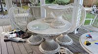 Full view of large round wicker table with metal top, two small round wicker side tables with glass tops, and two wicker fan chairs on a wooden porch.