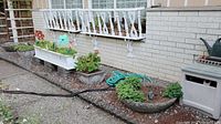 Photo showing two large round concrete planters and four rectangular metal and coir window box planters positioned along a building wall, some containing plants and soil.