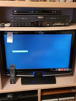 JVC 31-inch LCD TV showing screen on with remote placed on stand, JVC DVD player above TV, and GO.VIDEO 2-deck VHS player above DVD