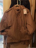 Beige/light tan Members Only quilted jacket hanging on a hanger. Front view of jacket with quilted texture, side pockets, and buttons/button flap lip detail.