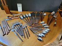 Full view of all 31 flatware pieces arranged on a wooden surface including forks, spoons, knives, and specialty utensils with wood handles and metal floral inlays.