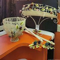 Demi-lune shelf, footed wire basket, and two towel racks displayed on an orange surface with visible painted metal roses and leaves on all pieces.