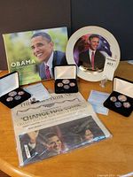 Wide view of all items including coins sets, certificates, commemorative plate, newspaper in protective bag, and book.