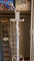 Tall white metal coat rack with 9 rounded hooks in room corner next to hanging shoe organizers