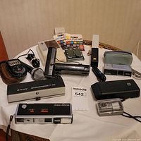 Wide shot showing the full lot including cameras, microphone with case, exposure meter in leather case, film splicers with splice tapes, and projector pointer.