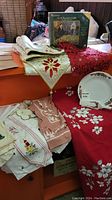 Overview of red embroidered tablecloth, multiple runners, Christmas plate and cake server set arranged on orange boxes.