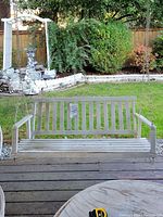 Front view of wooden porch swing hanging from chains on a deck with garden background.