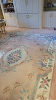 Large 100% wool Chinese area rug with floral pastel design on the floor showing worn fringe.