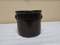 Front view of antique brown glazed ceramic crock with smooth shiny surface and handles on side