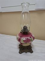 Full view of antique oil lamp showing cast iron base, floral painted milk glass bowl, and glass chimney.