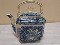 Side profile of blue and white square ironstone teapot with detailed landscape and floral border.