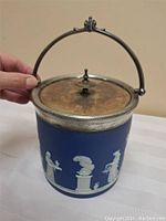 View of the biscuit barrel showing the cobalt blue jasperware body with white classical relief decorations and silver plated lid with handle.